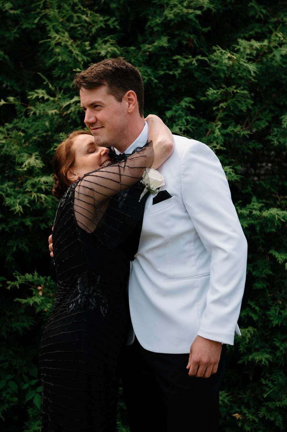 A couple shares an intimate moment in front of lush green foliage.