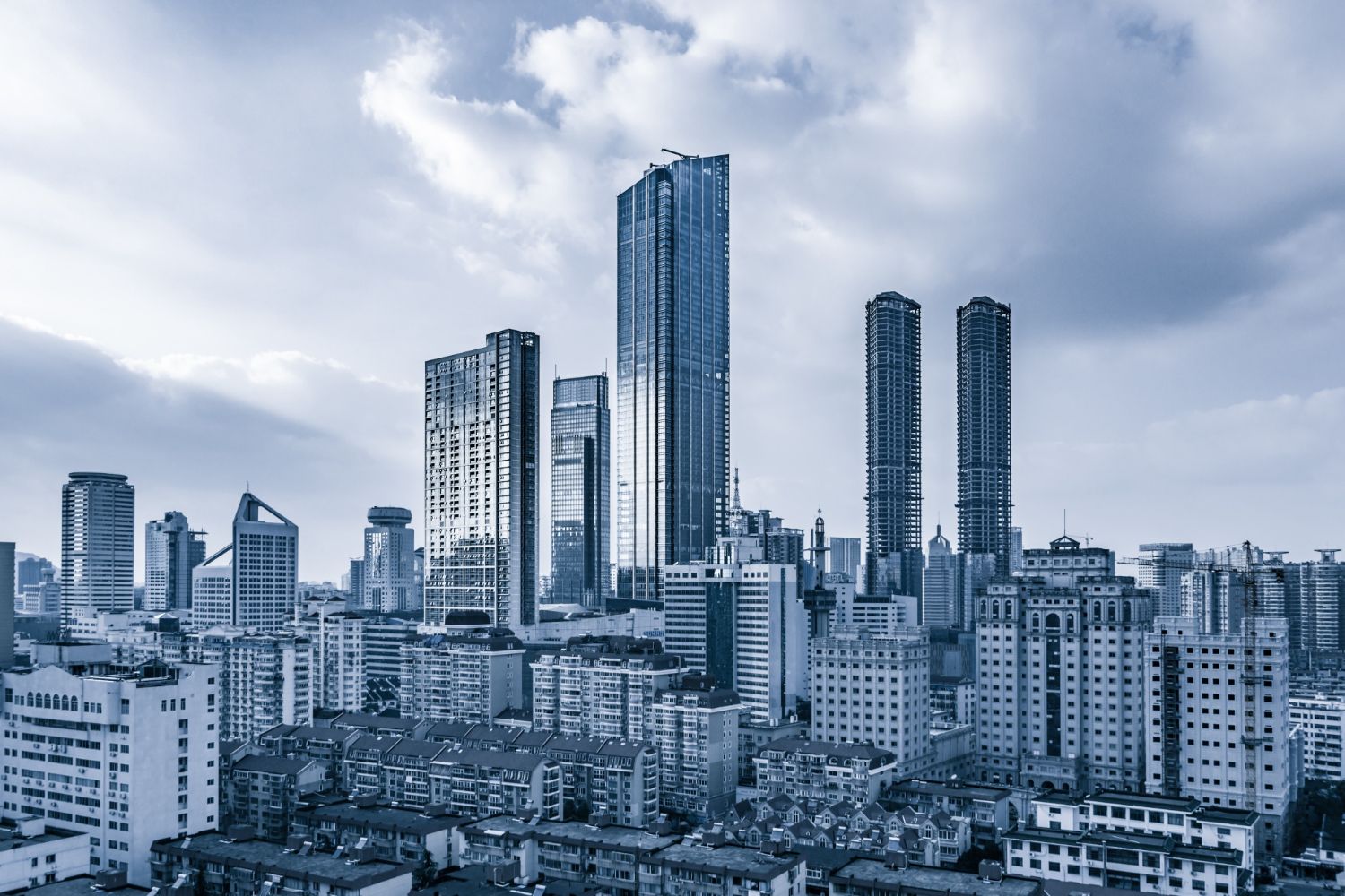 Modern cityscape with tall blue-tinted skyscrapers against cloudy sky.
