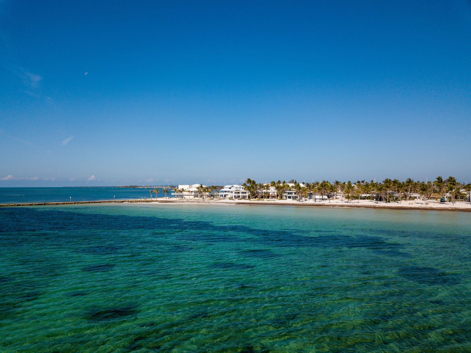 Aerial view of a tropical beach resort with turquoise waters and palm trees.
