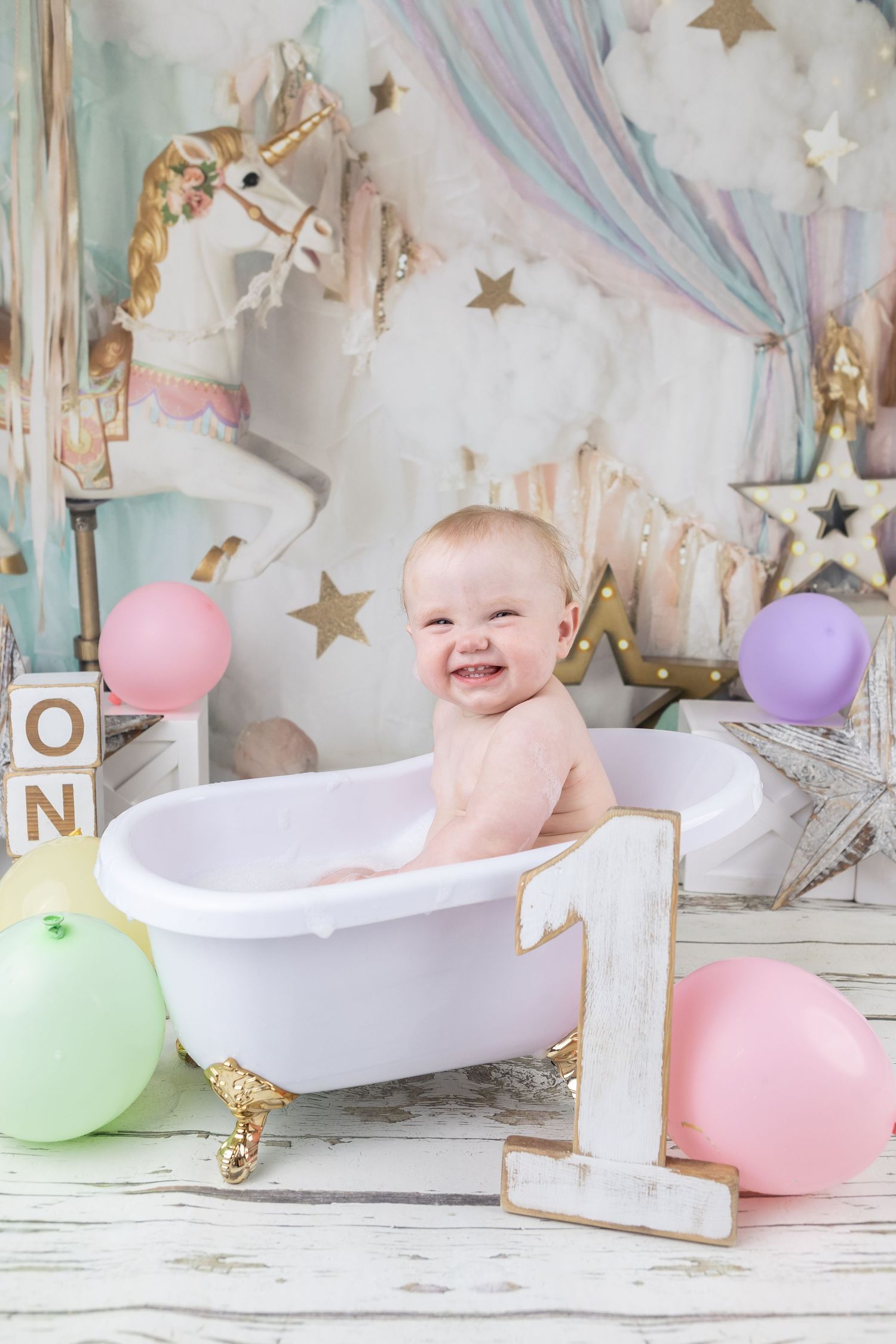 Cake smash photo session with pastel balloons, stars and white bathtub props.