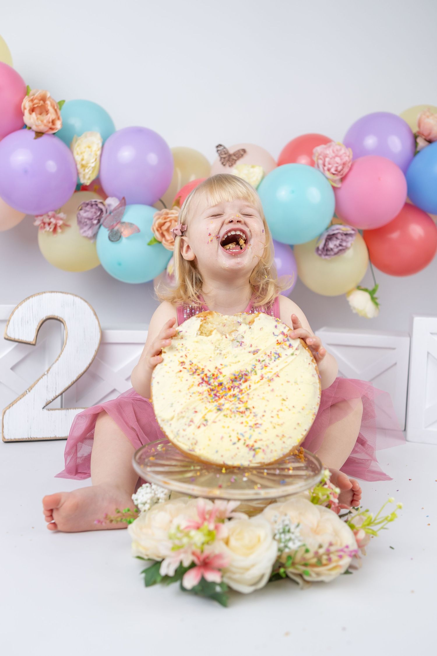 First birthday cake smash photography with colorful balloon garland and sprinkled donut prop.