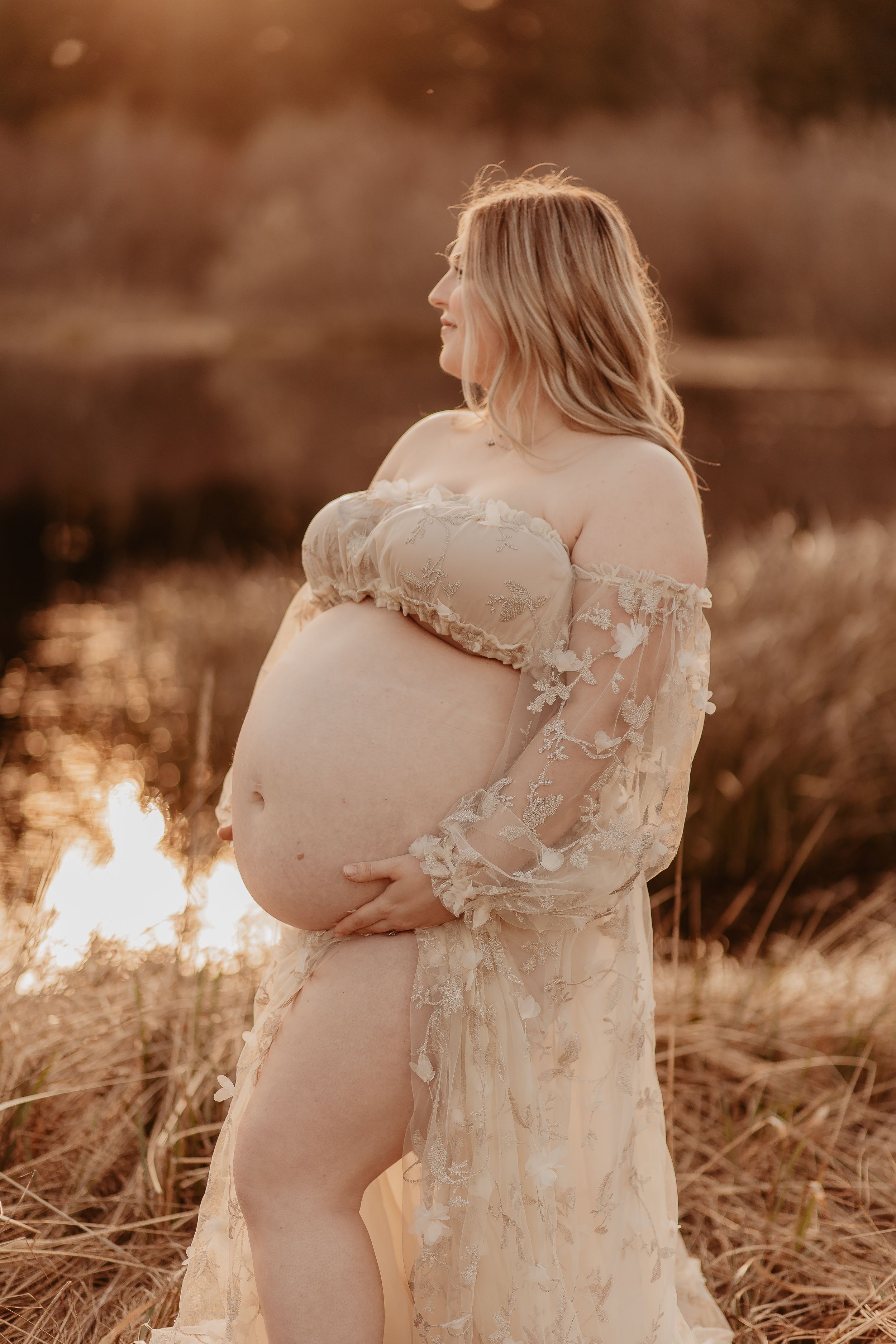 Intimate maternity photography session in a field at sunset with soft sepia tones.