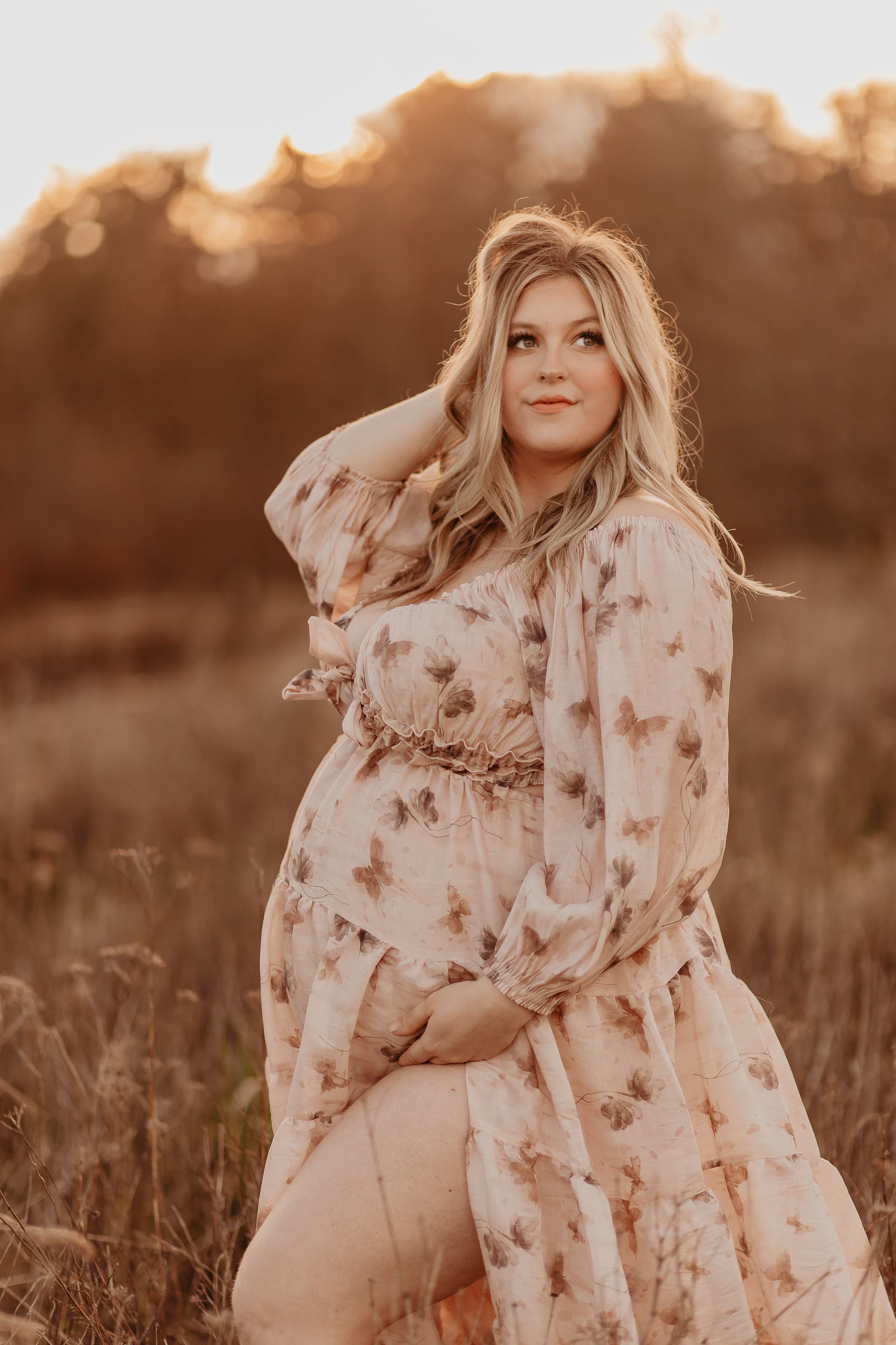 Maternity portraits in a sun-drenched field with floral dress during golden hour.