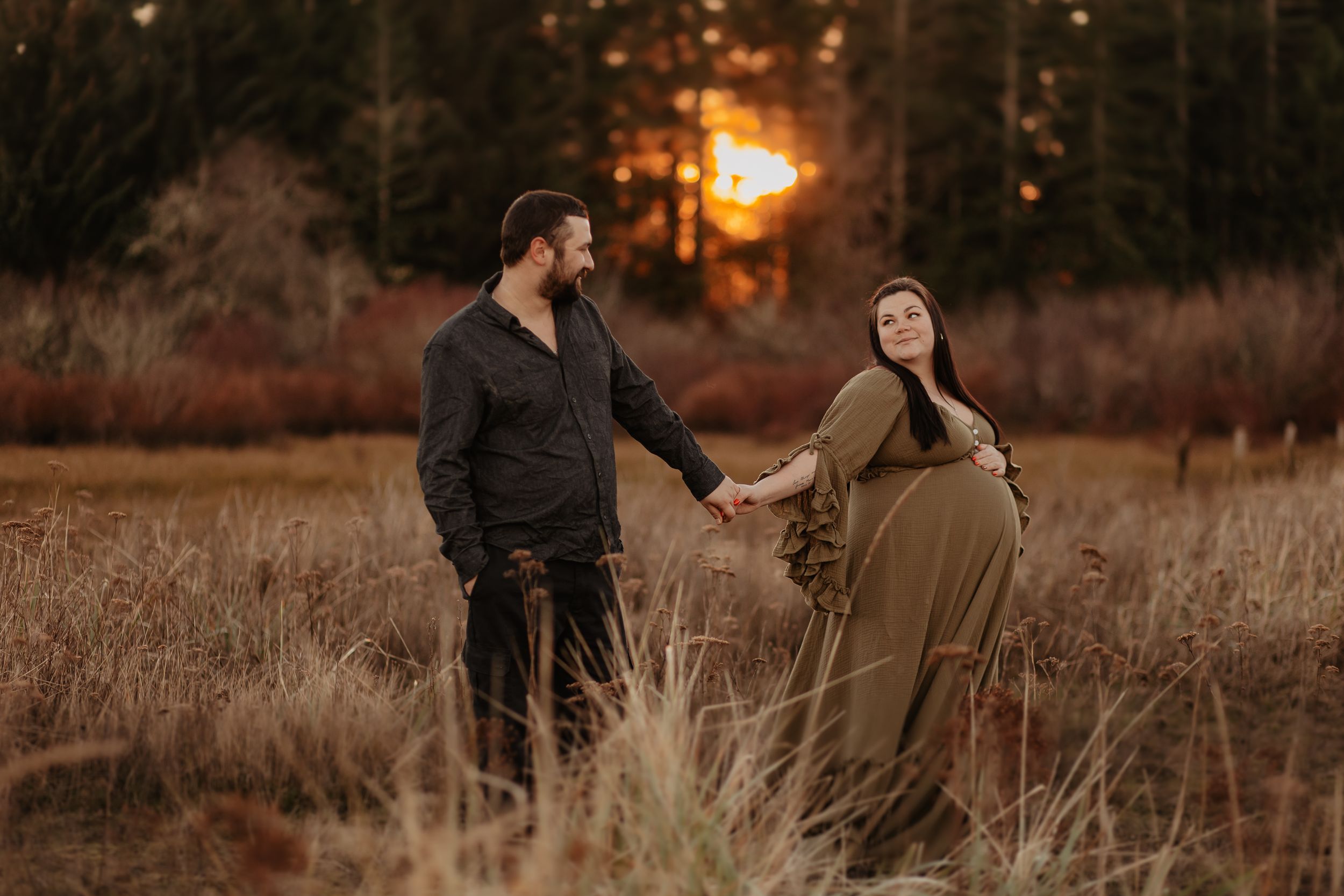 A couple walks through a golden field at sunset with warm autumn lighting and tall grass.