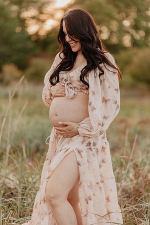 Maternity session in a grassy field during golden hour with flowing floral dress.