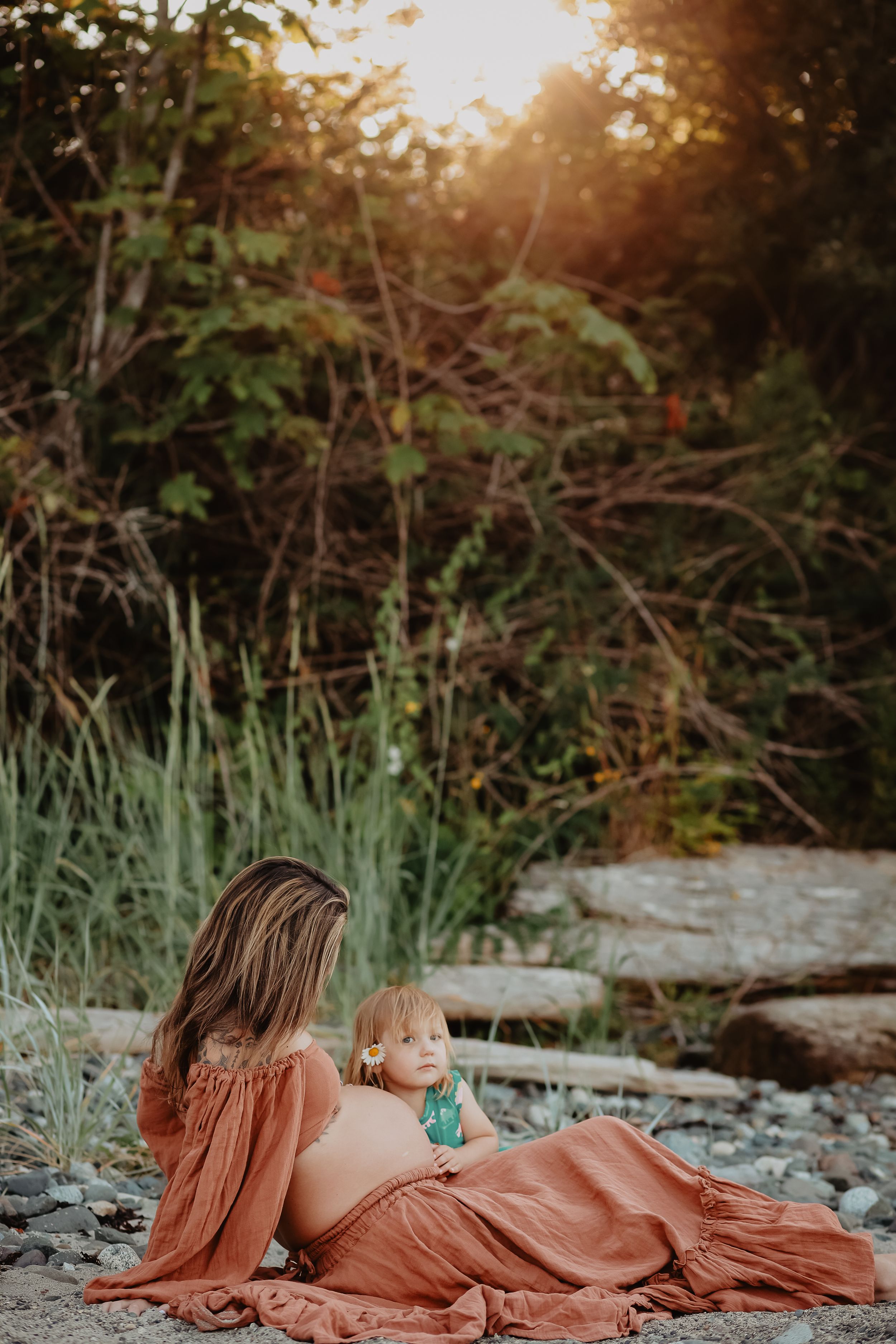 Intimate maternity session on rocky beach at sunset with flowing terracotta dress.