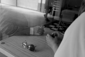 Black and white photo showing marbles on a wooden table while hands can be seen playing a game.