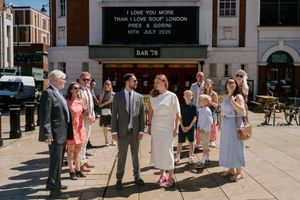 Wedding party stands outside theater with marquee displaying love quote overhead on sunny day.