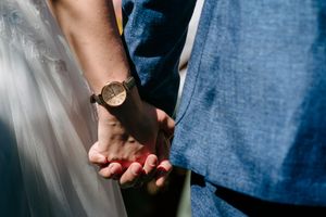Close-up shot of hands holding together with one person wearing a gold watch and red nail polish.