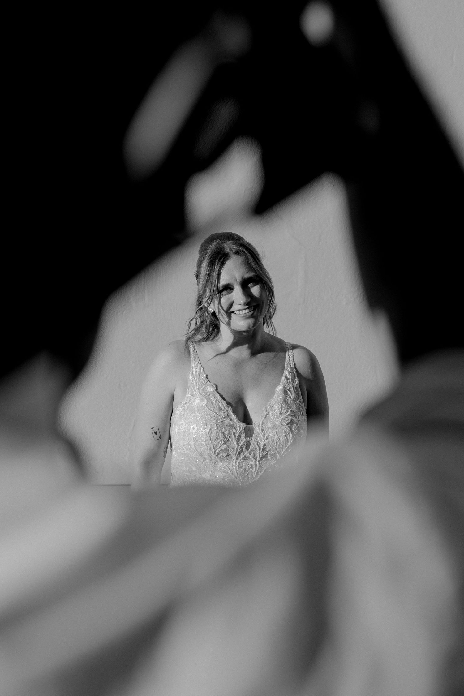 Artistic black and white portrait taken through leaves showing a person in a lace wedding dress.