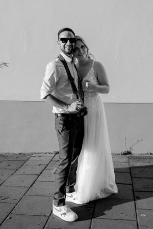 Black and white photo of a couple on their wedding day posing together against a plain wall.
