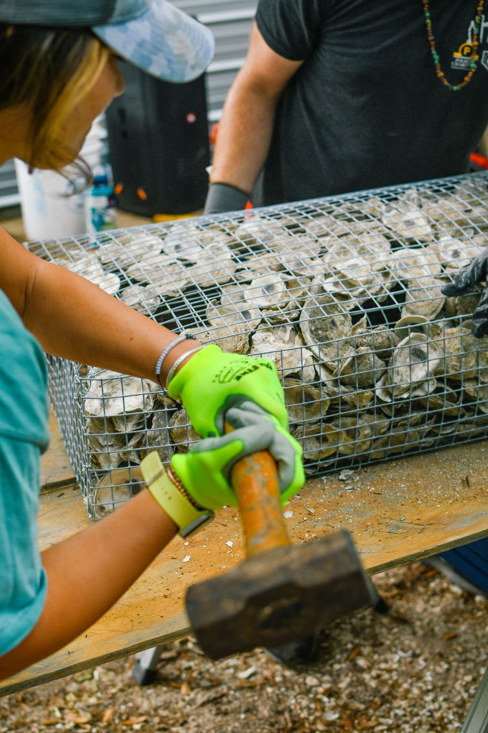 Hands in protective gloves working on metal mesh container with tools.