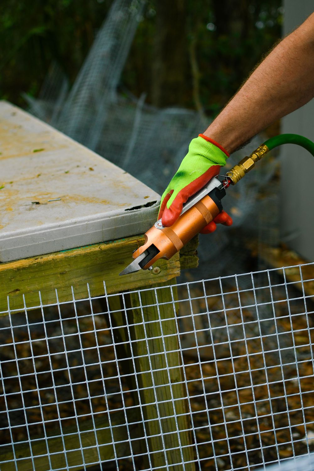 Close-up of gloved hand using tool on wire mesh construction.