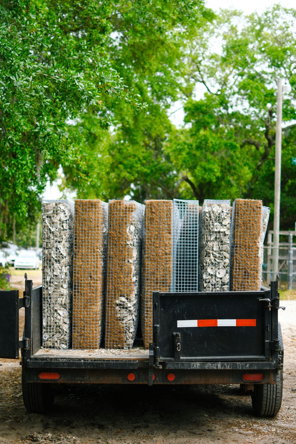 Stacked rolls of metal fencing materials and rocks loaded on a dark trailer outdoors.