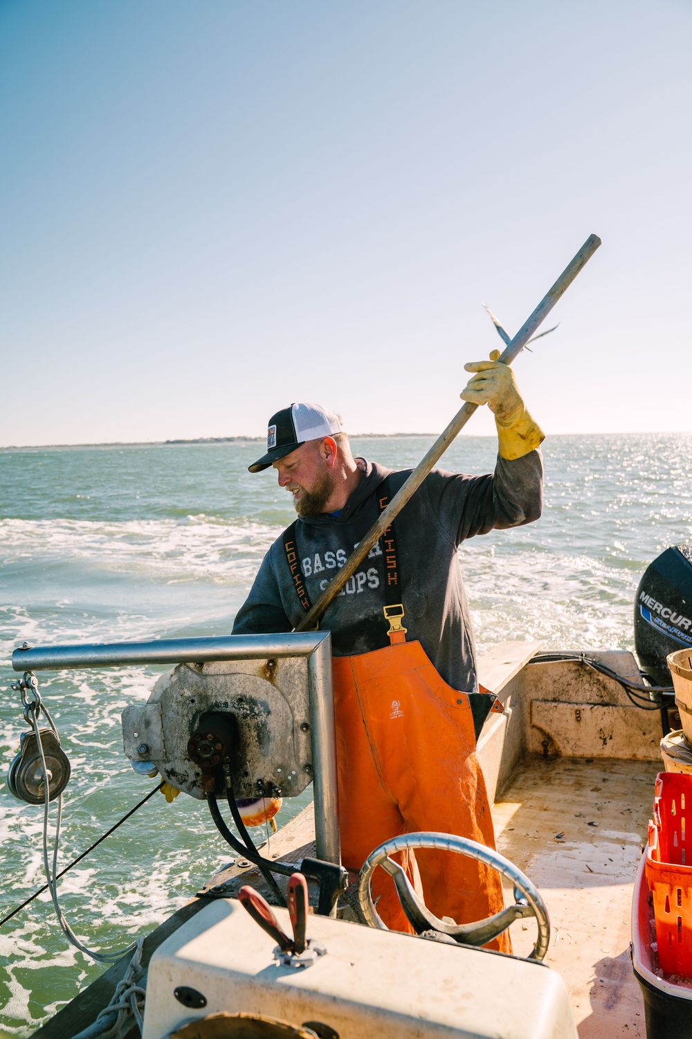 Commercial fisherman working on a boat deck with orange safety gear against a bright ocean backdrop.