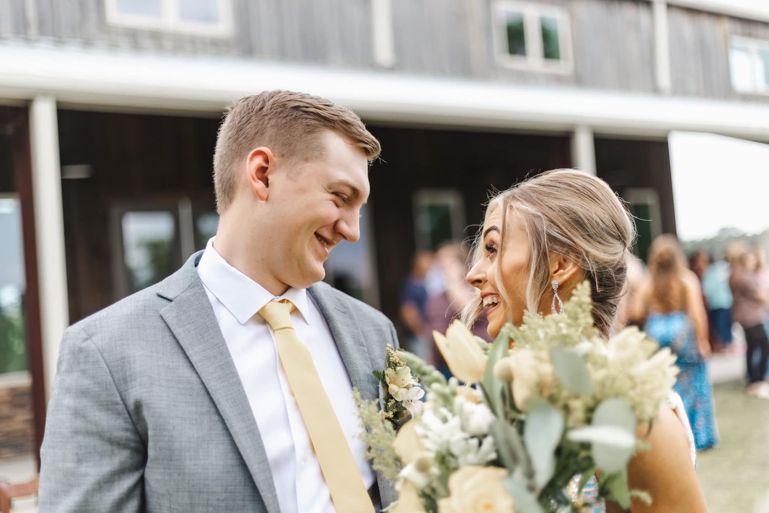 Wedding party members walk along a pathway together while holding bouquets of white and green flowers.