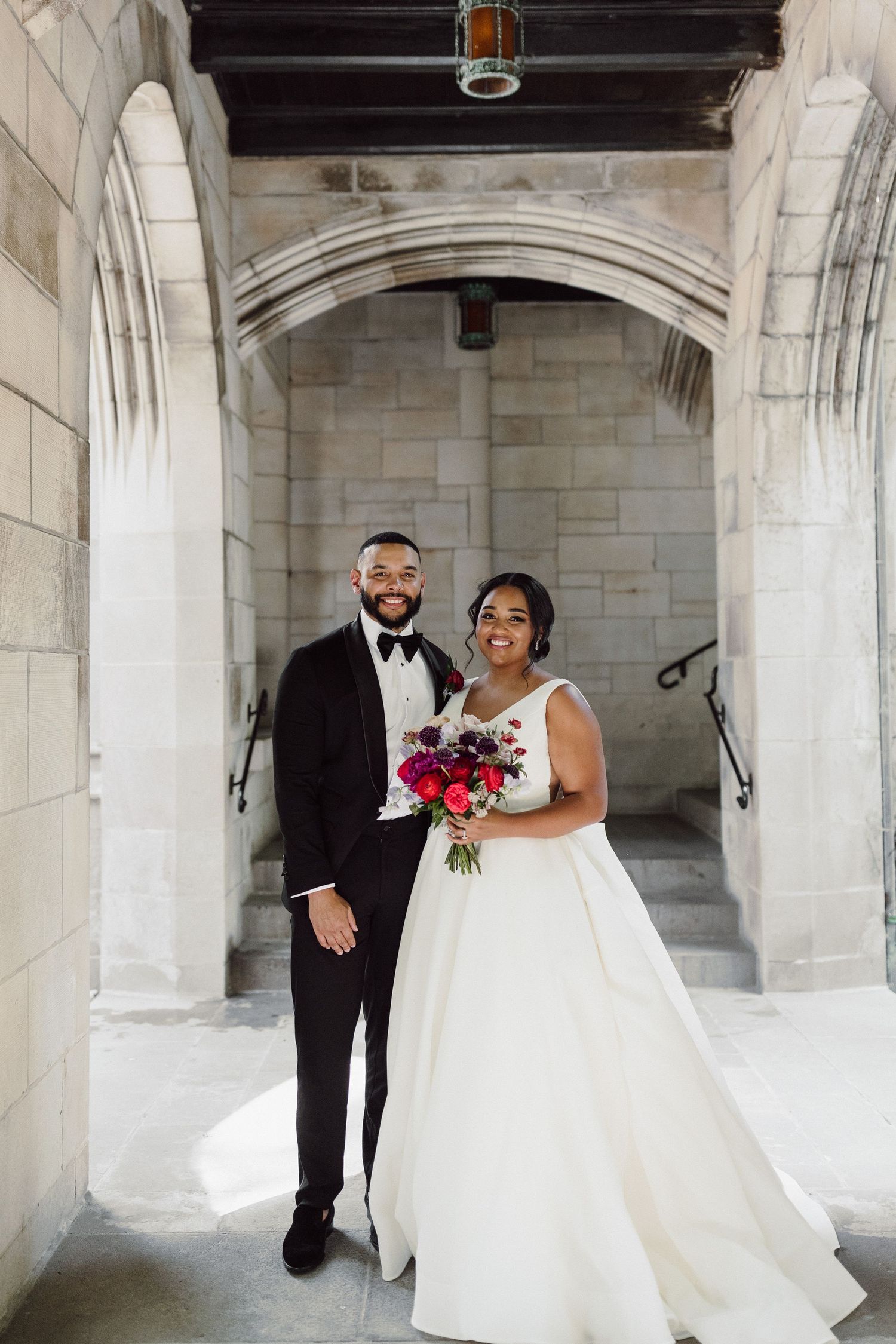 Wedding couple poses together under elegant stone archways with natural lighting.