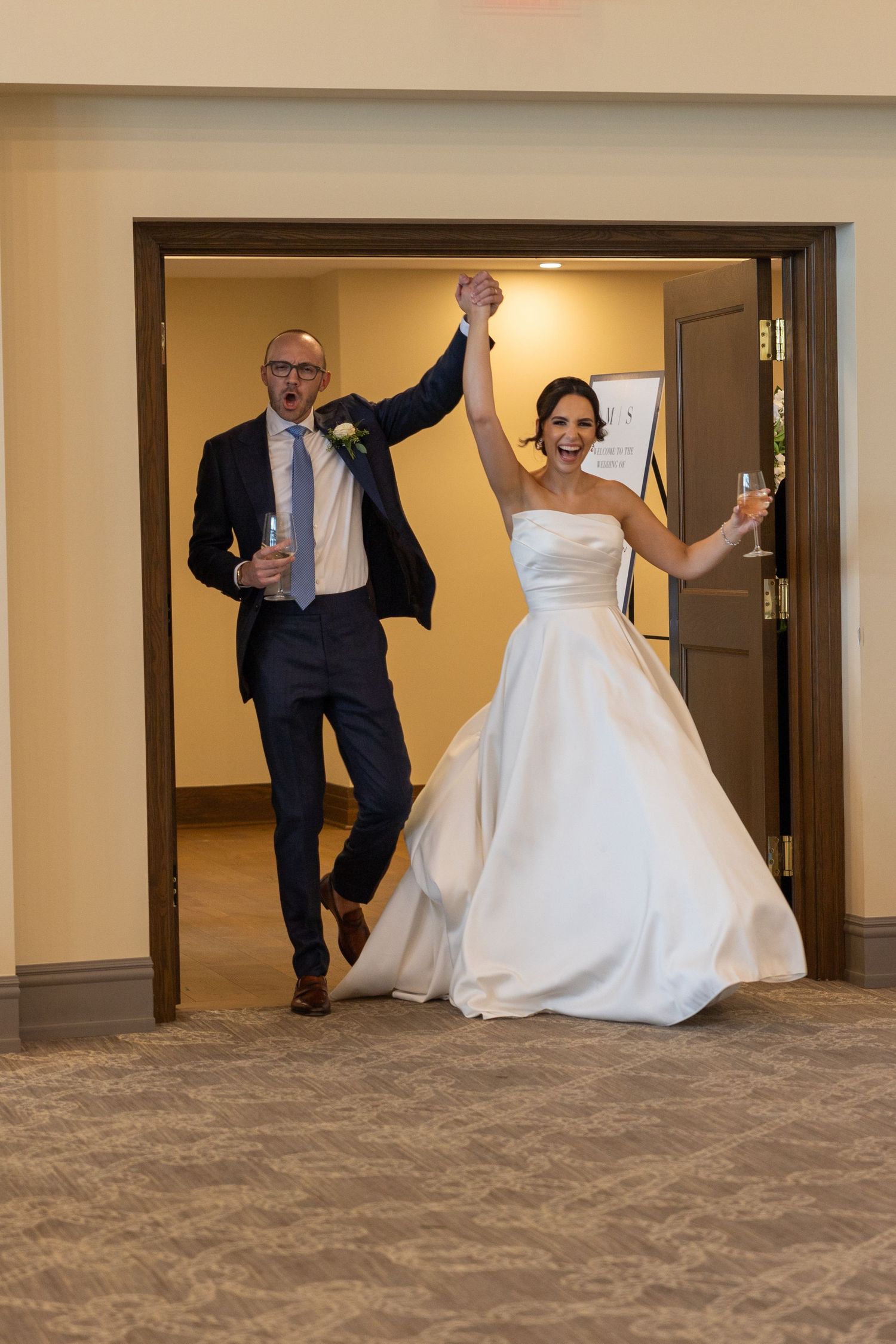 Couple walks into their reception with arms raised and champagne, captured by wedding photographer Rachel Martinez Photography Novi, MI