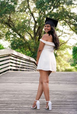 Young woman in white dress and graduation cap posing on wooden bridge.