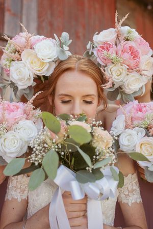 Wedding bridesmaids hold elegant bouquets of pink and white roses with eucalyptus and baby's breath accents.