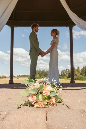Floral bouquets rest on ground while a silhouetted couple shares a wedding moment under a covered pavilion.