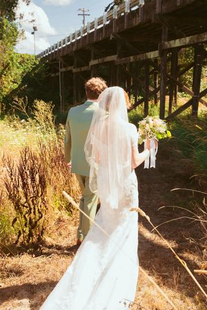 Wedding dress flowing in the wind against a rustic bridge backdrop on a sunny day.