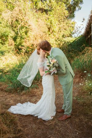 Intimate wedding moment captured in golden sunlight with flowing white dress and mint green suit.