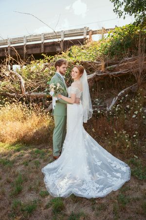 Elegant wedding couple photographed outdoors with a beautiful lace train dress and sage green suit.