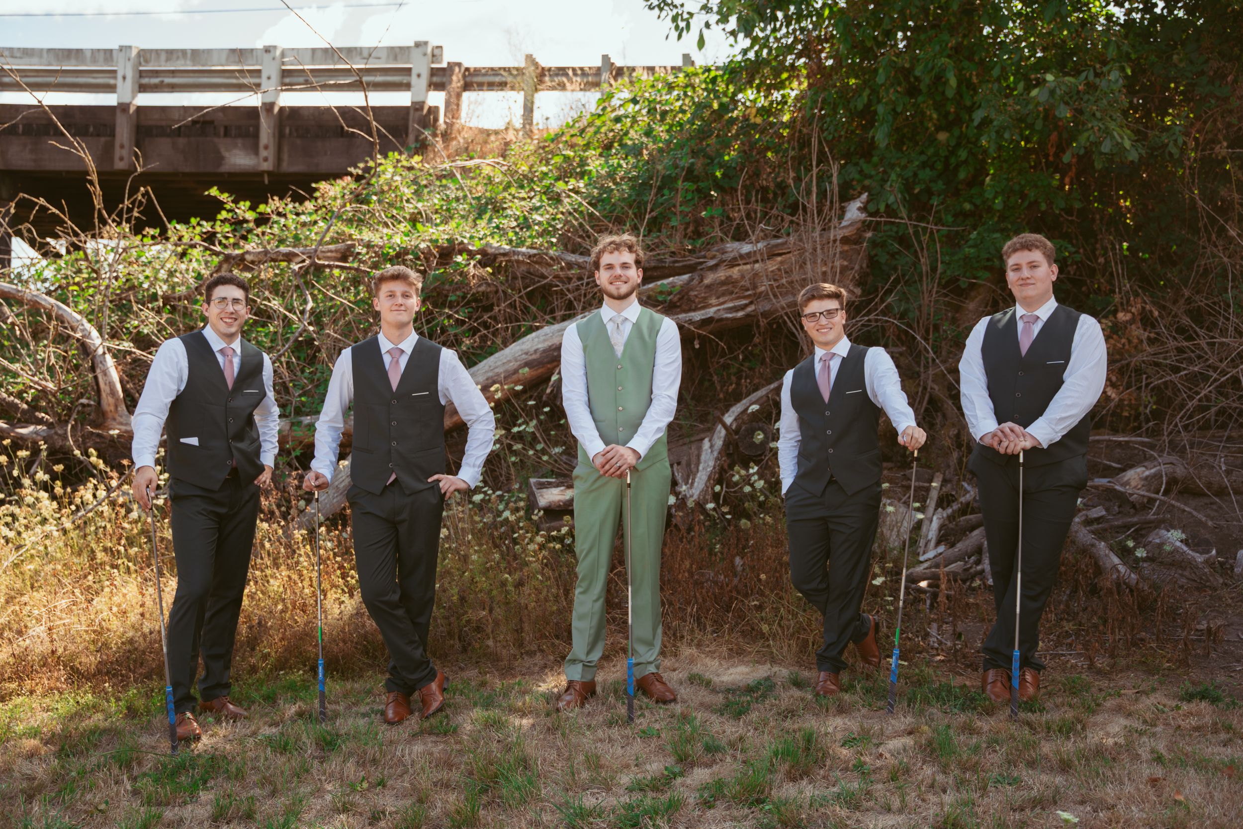 Wedding party in mint green vests and suits pose together outdoors in natural setting.