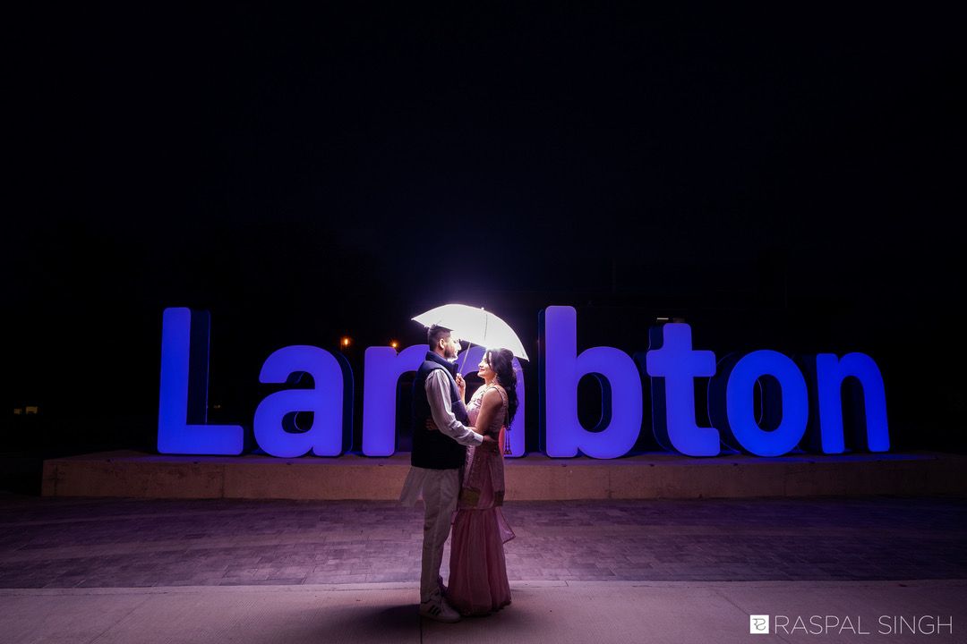 A couple poses romantically in front of illuminated blue Lambton signage at night.