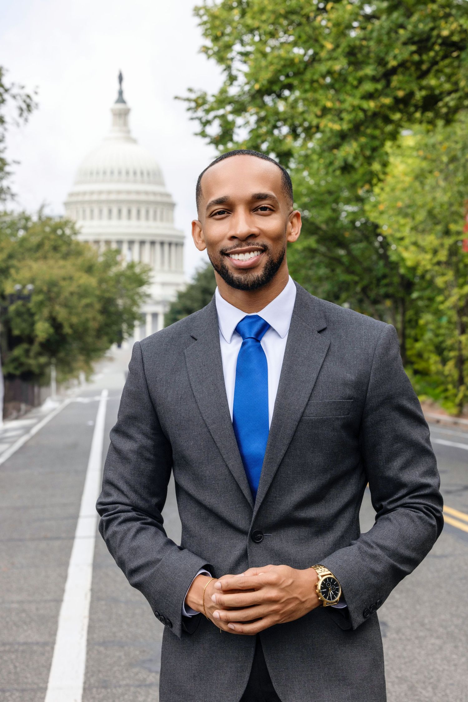 Professional photo of someone in a grey suit and blue tie standing in front of the US Capitol building.