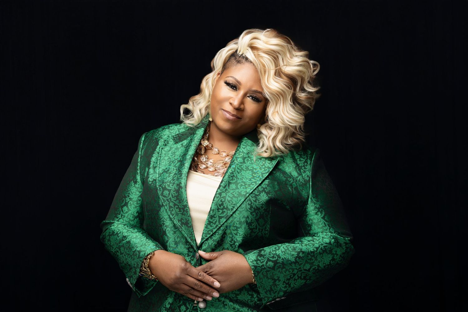 Glamorous portrait of someone wearing a sparkling emerald green blazer against a black background.