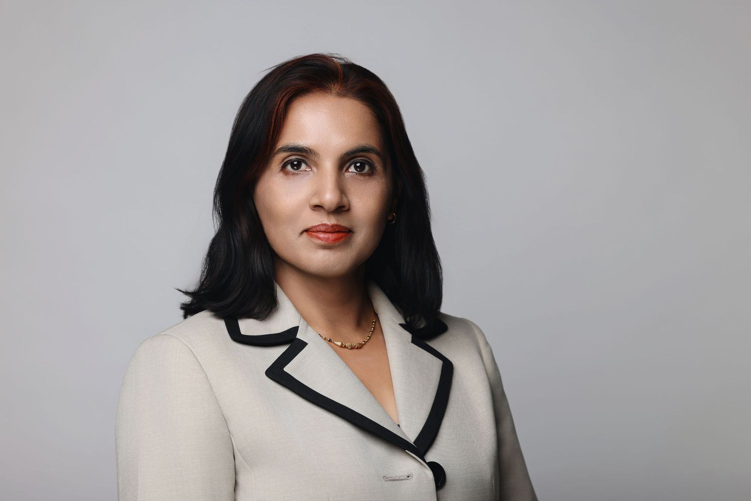 Professional headshot against gray backdrop of person wearing white blazer with black lapels.