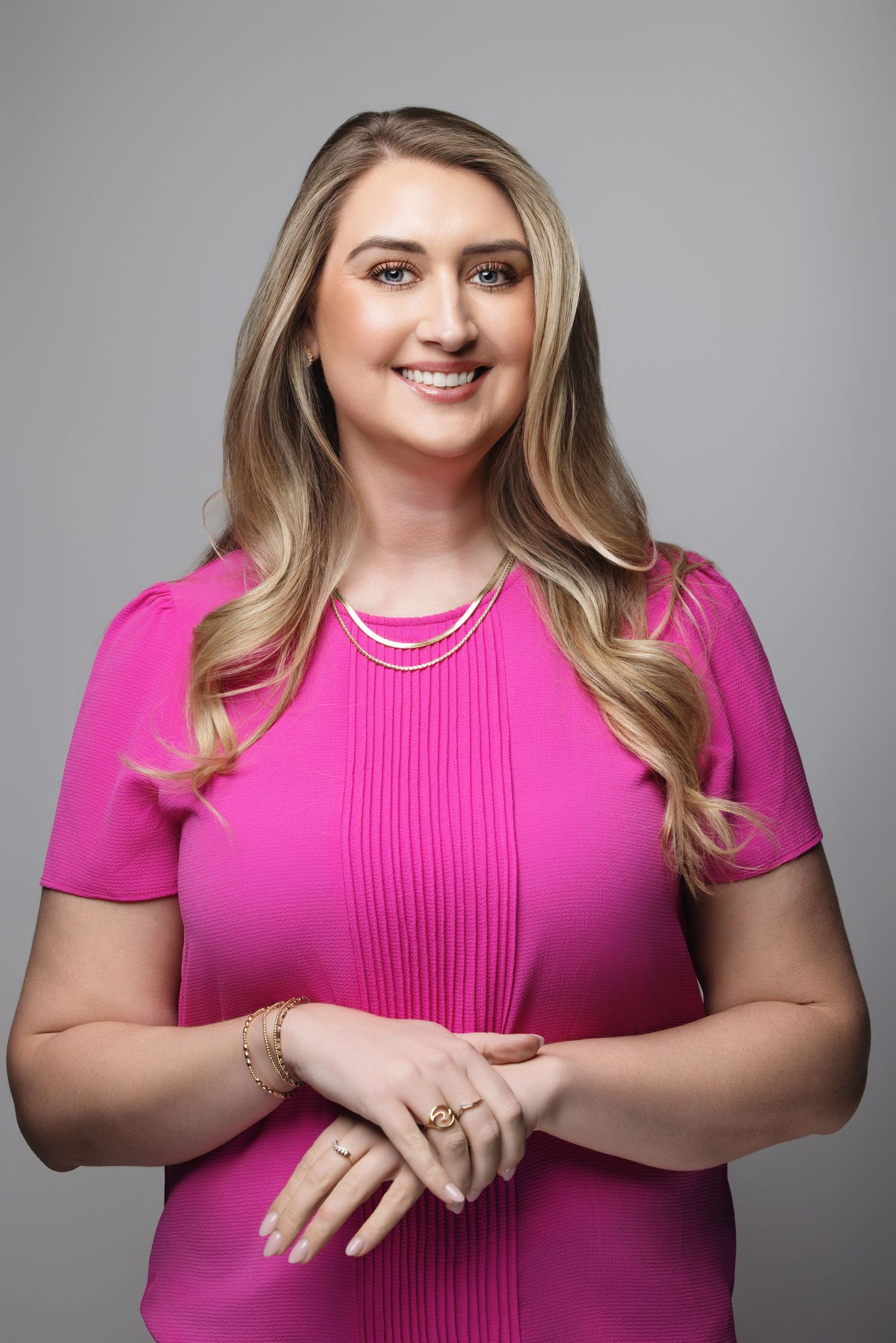 Person in bright pink pleated dress poses confidently against gray studio background.