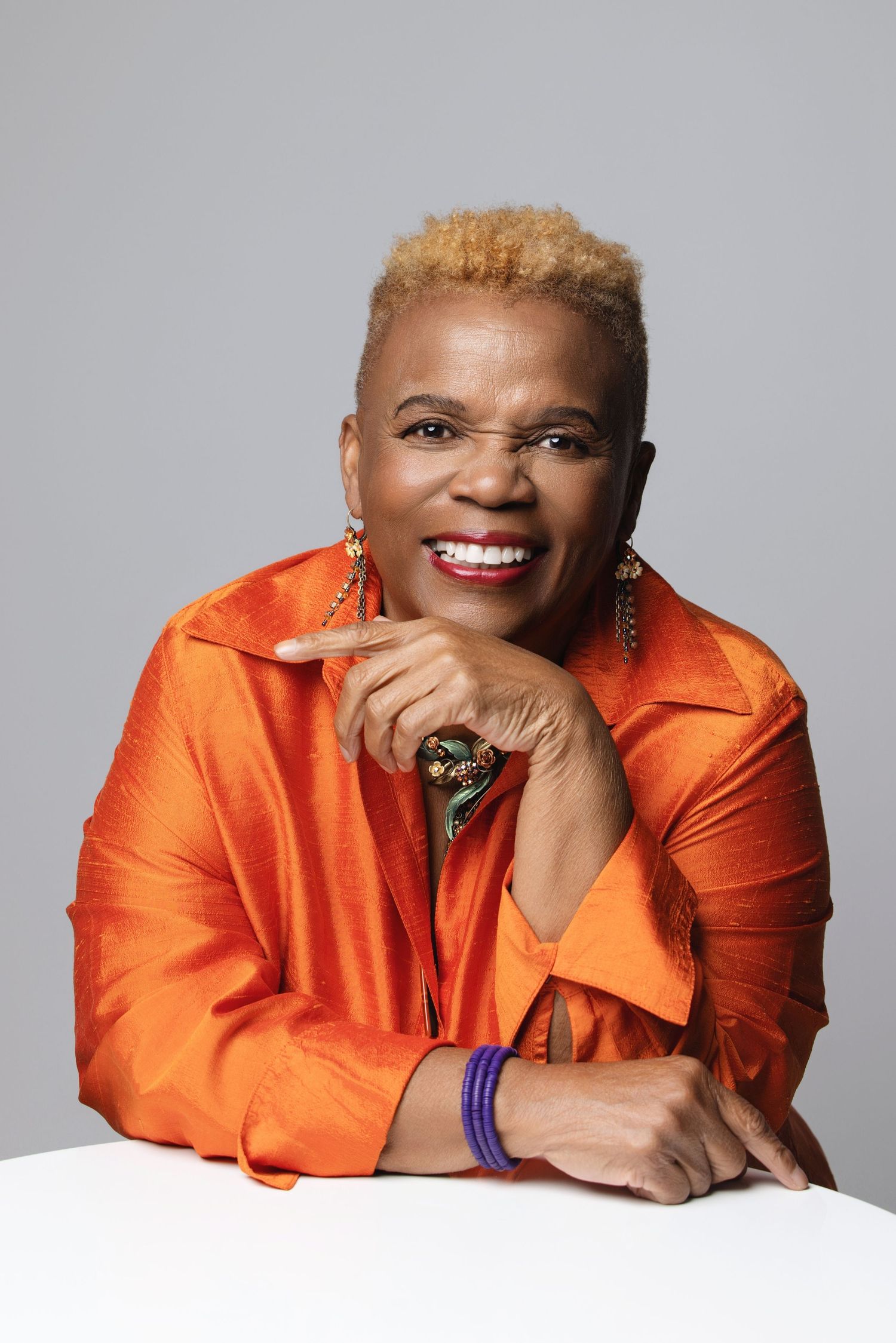 Person wearing bright orange blazer poses in multiple angles against light gray backdrop.