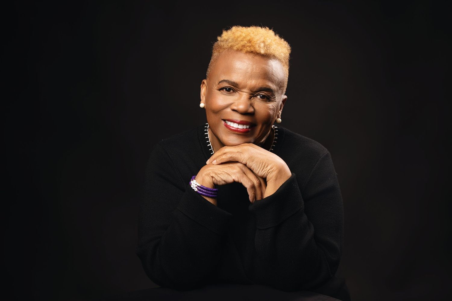 Person in black attire poses thoughtfully against dark background in professional headshots.