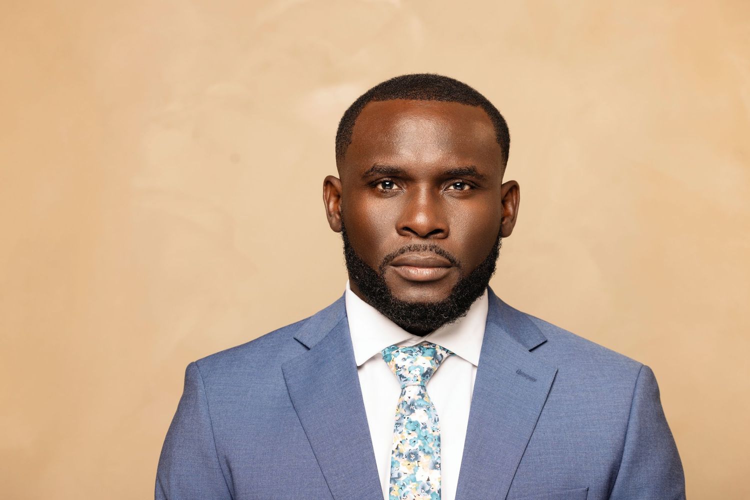 Professional headshots of someone wearing a gray suit and patterned tie against a neutral background.