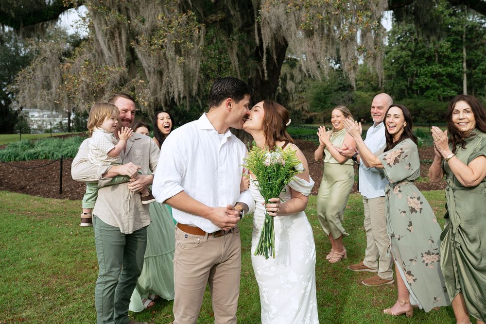 Wedding guests celebrate with joyful laughter in a garden setting with Spanish moss hanging from trees.