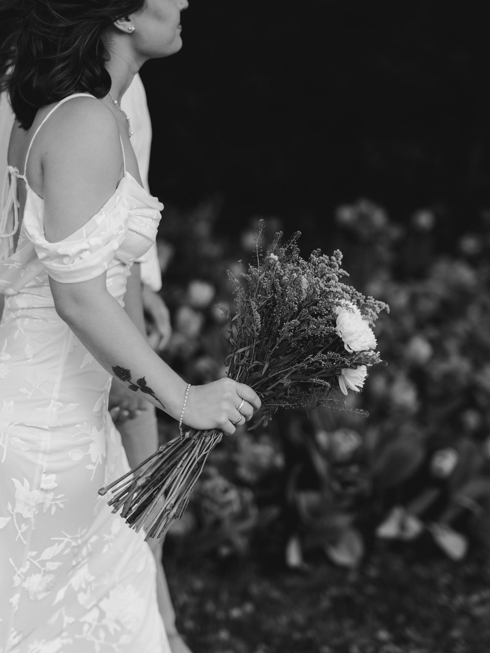 A person in a white wedding dress holds a rustic bouquet of dried flowers in a black and white photograph.