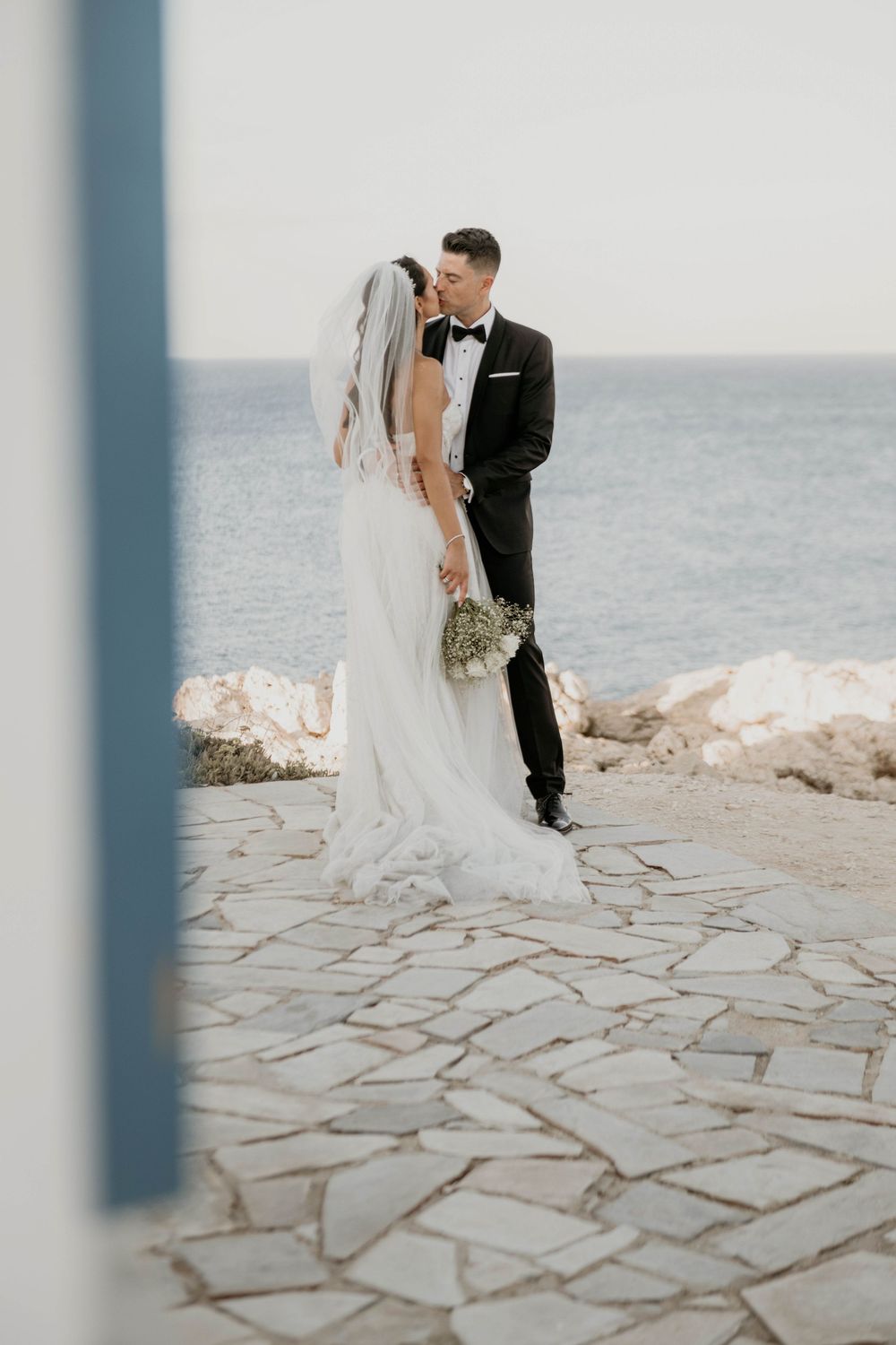 A bride and groom share an intimate moment while standing on a stone patio overlooking the ocean.