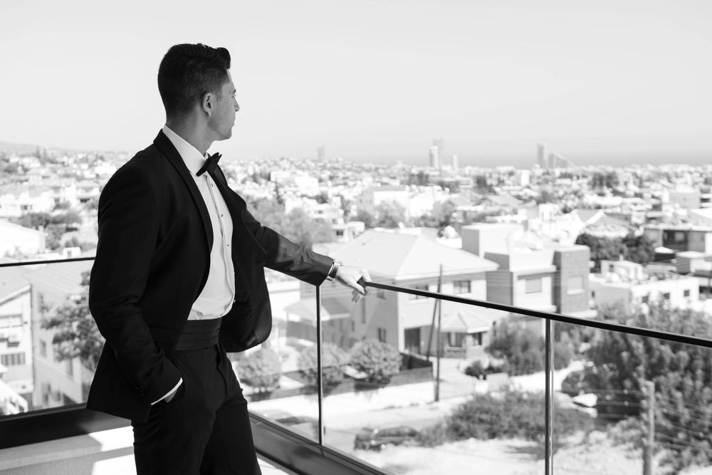 A person stands on a rooftop balcony gazing at a cityscape of buildings and towers stretching to the horizon.