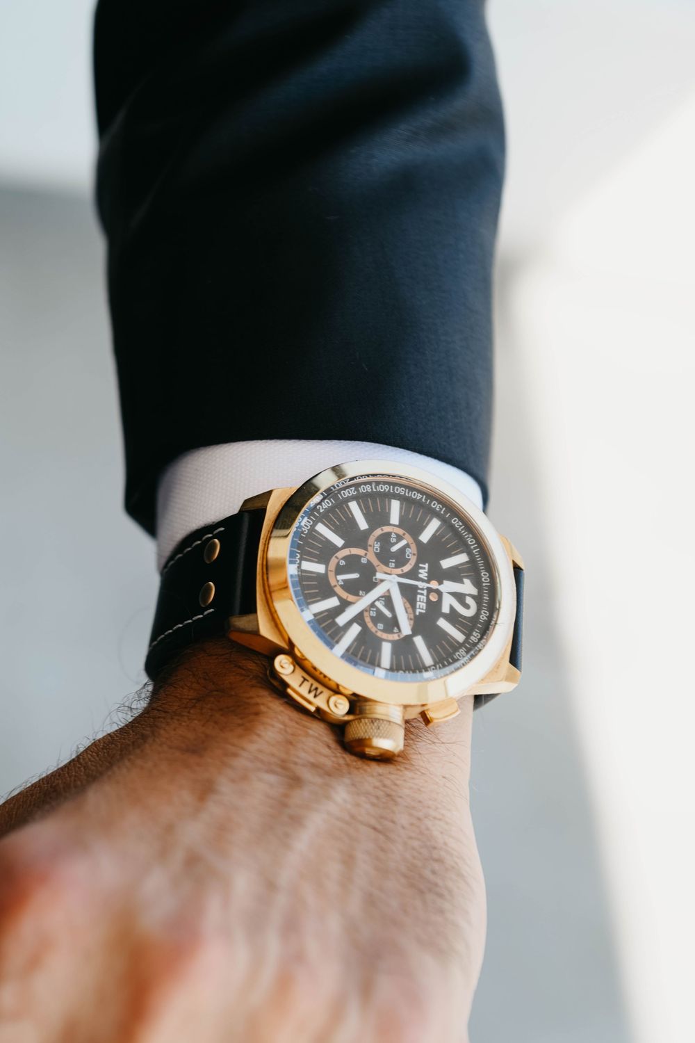 Close-up view of a luxury chronograph watch with gold accents and black leather strap worn on wrist.