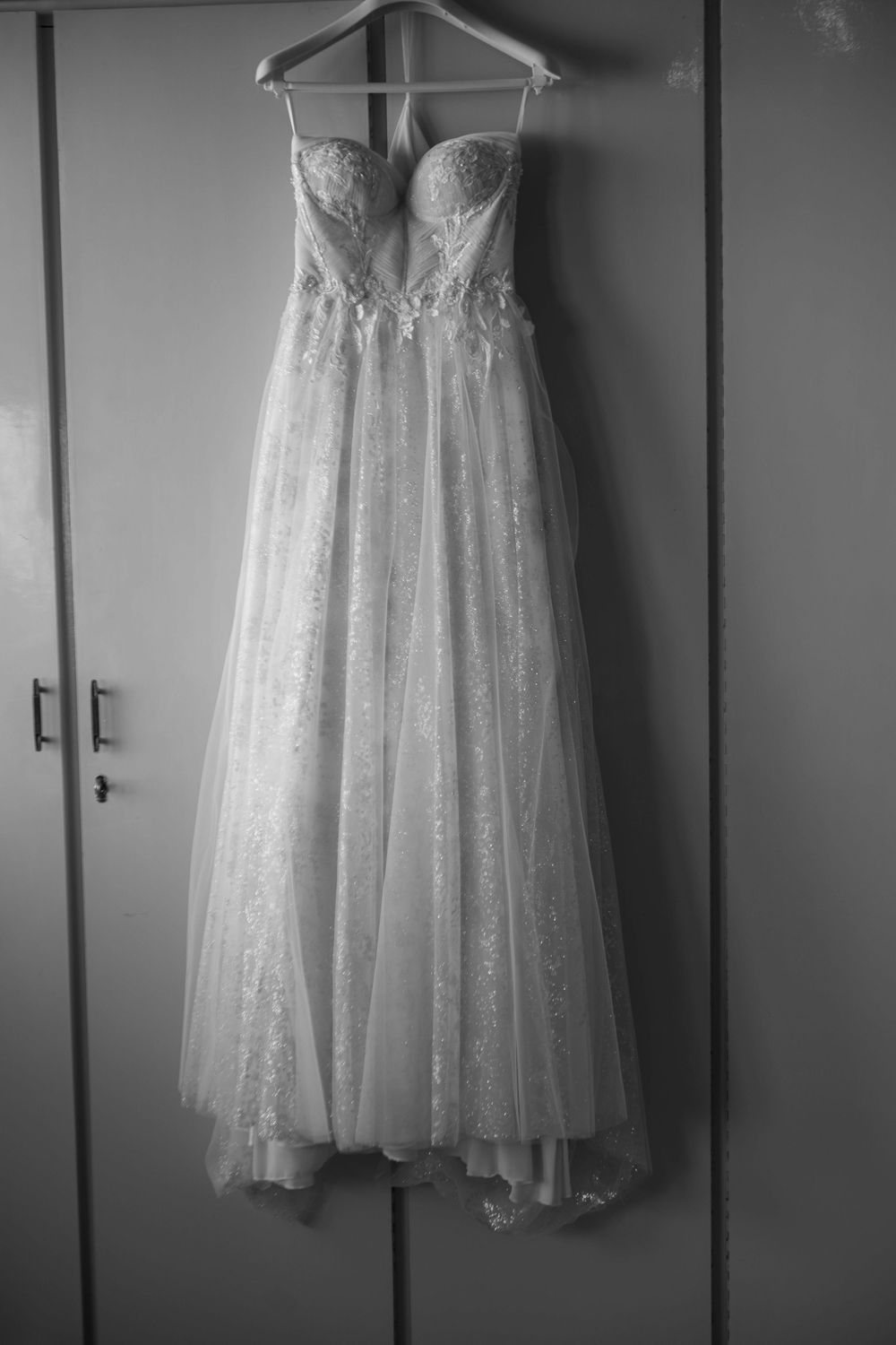 A stunning white wedding dress with lace details and tulle skirt hangs elegantly on a hanger against a grey wall.