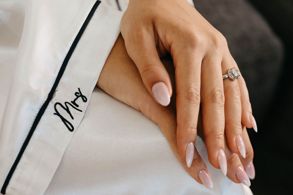 Woman's hands with neutral manicure writing in an open notebook with a black pen on white desk.