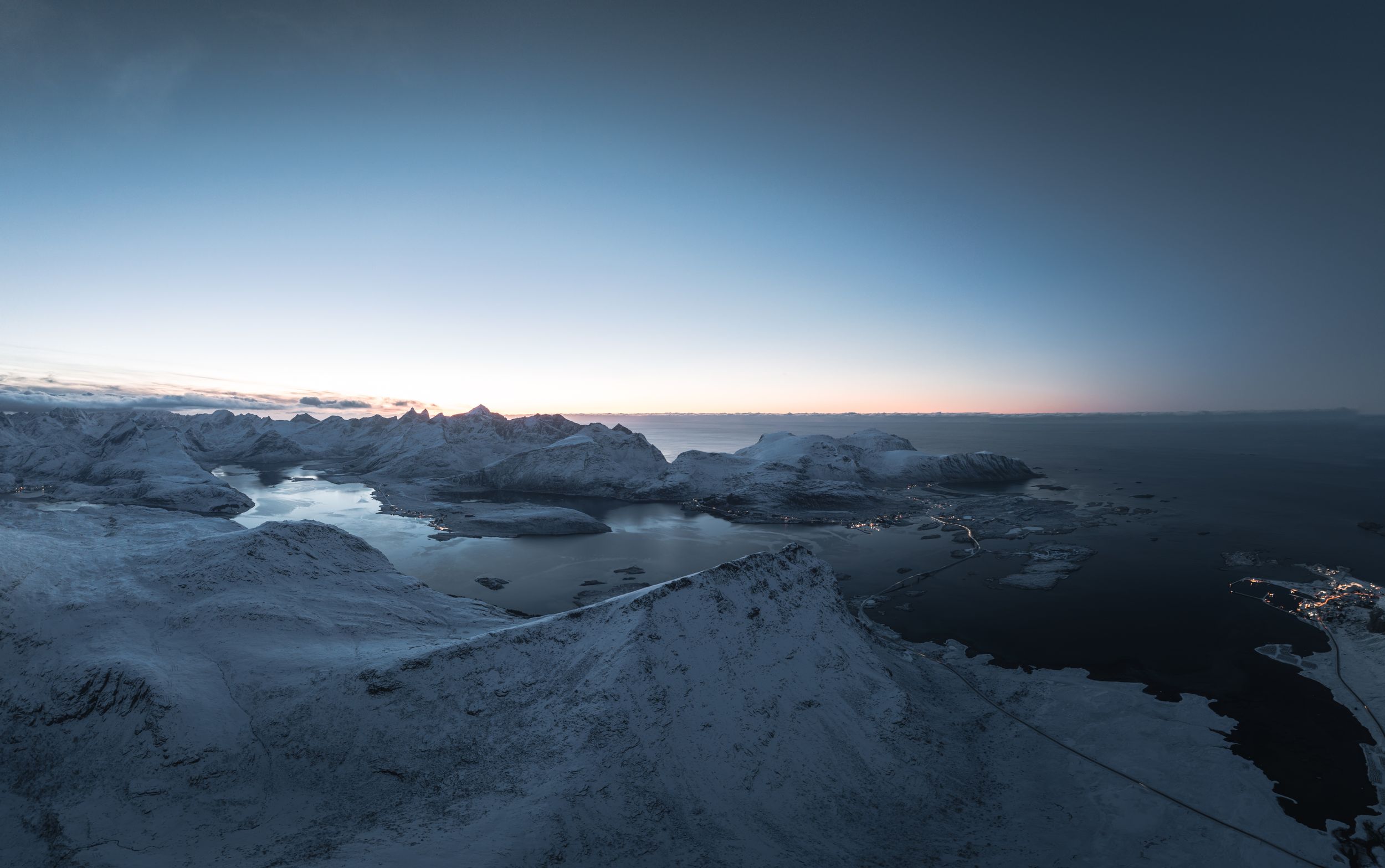 A dramatic winter landscape shows snow-covered rocky terrain against a dusky horizon and dark ocean waters.
