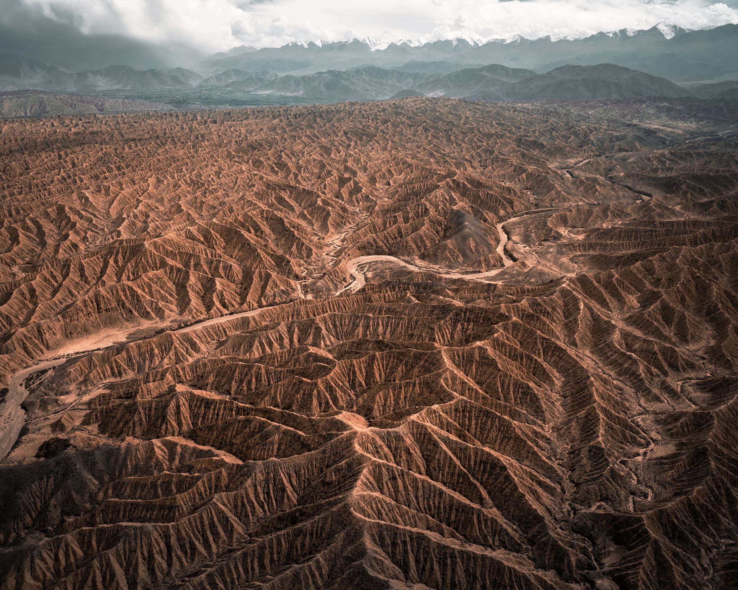 Aerial view of winding dirt roads snaking through rugged desert badlands under dramatic cloudy skies.