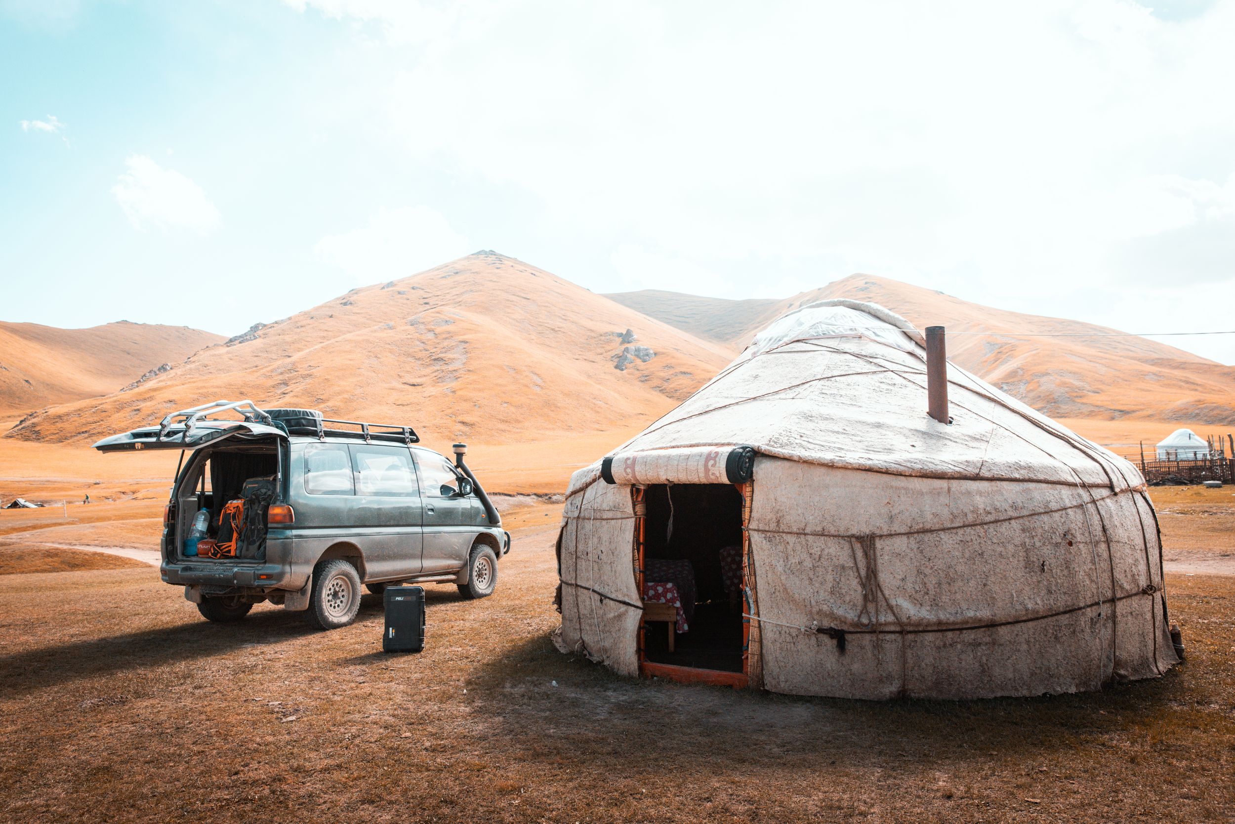 Traditional white yurt tent dwellings stand against a backdrop of orange sand dunes in a desert landscape.