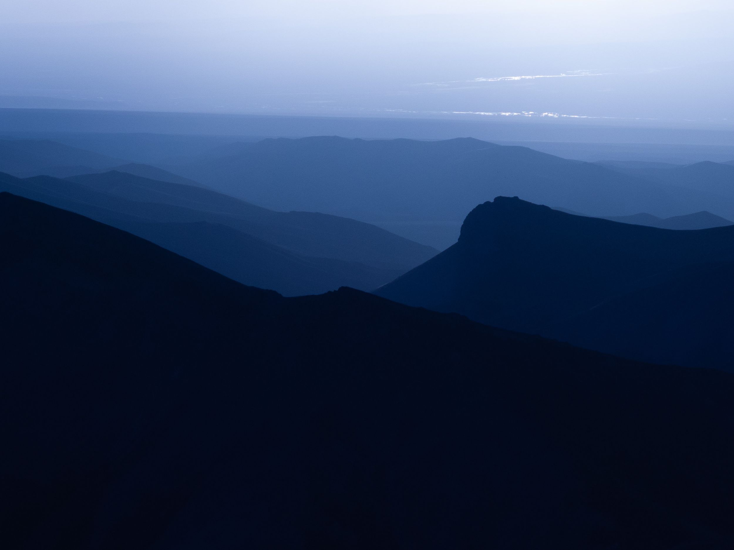 Silhouetted mountain ridges fade into misty blue layers beneath a dusky evening sky.