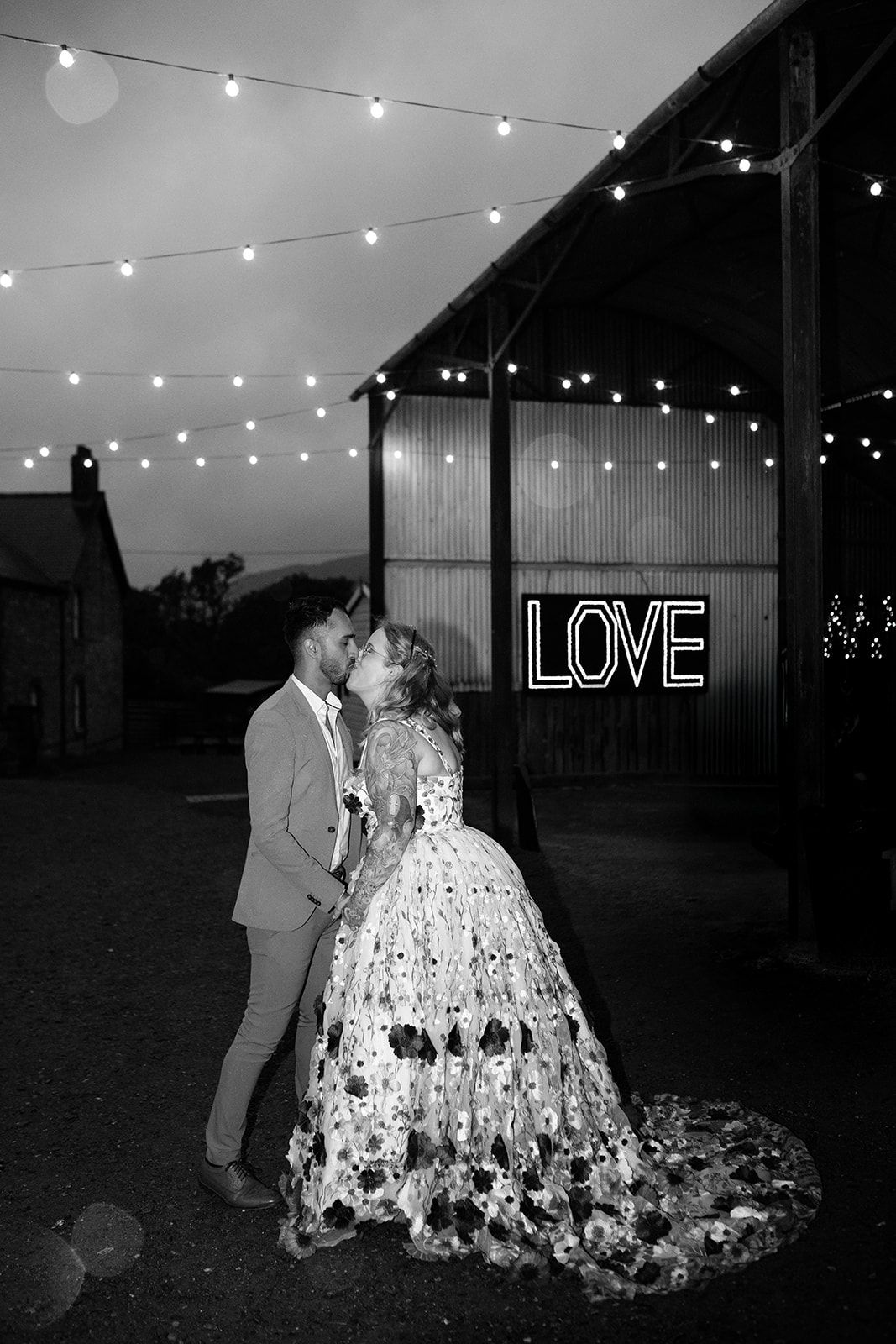 Evening wedding reception with string lights and neon LOVE sign creating romantic ambiance.
