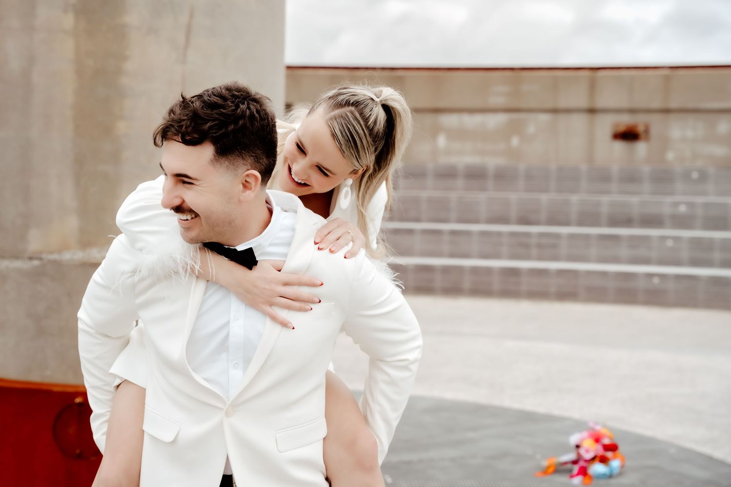Playful wedding portrait with couple in white sharing a joyful piggyback moment.